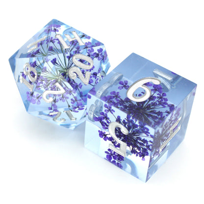 Fleur de Lilas is a 7-piece set of lavender sharp edge resin dice with tiny purple flower inclusions, inked in silver.