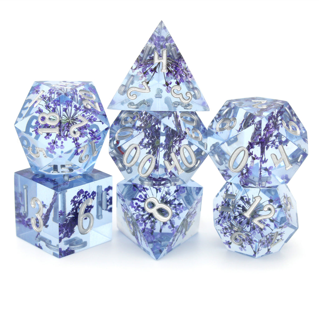 Fleur de Lilas is a 7-piece set of lavender sharp edge resin dice with tiny purple flower inclusions, inked in silver.