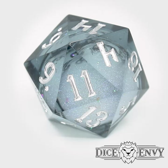 Snow Globe is a 7-piece, translucent grey-blue resin dice set with a liquid core of snow white glitter, inked in bright silver.