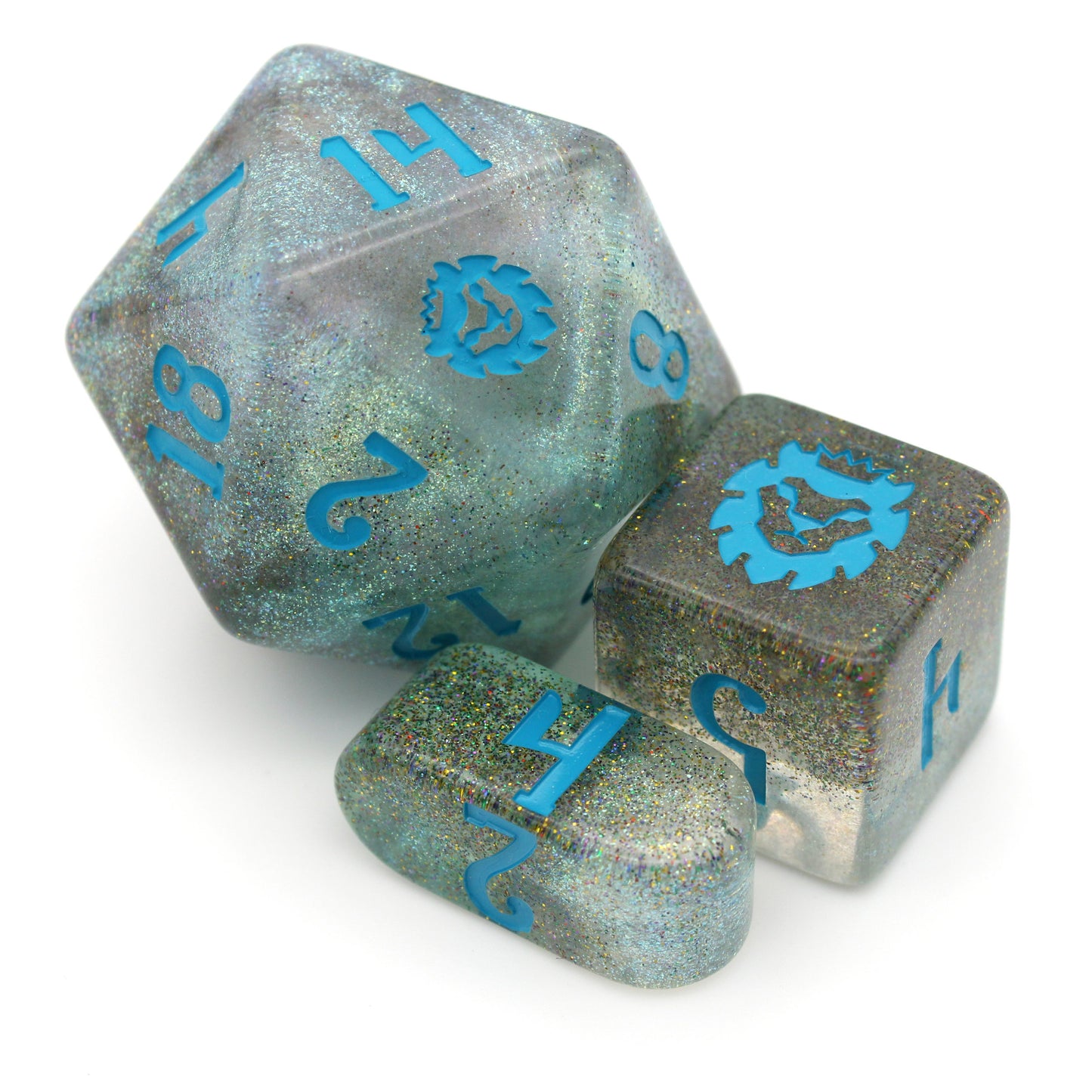 A closeup on a chonky d20, d6, and infinity d4 from River Magic, a 10-piece dice set of swirling blue, brown, and clear resin, shot through with silver glitter and inked in teal.